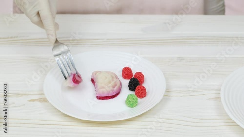 Rose shaped jelly dessert made from raspberries and cream in a white plate on a white wooden table. Chef cuts and taste the dessert.