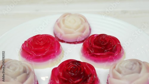 Rose shaped jelly dessert made from raspberries and cream in a white plate on a white wooden table.