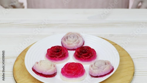 Rose shaped jelly dessert made from raspberries and cream in a white plate on a white wooden table. The chef puts a plate of dessert on the table. Round wooden board.