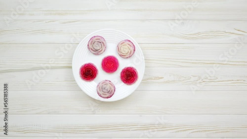 Rose shaped jelly dessert made from raspberries and cream in a white plate on a white wooden table.