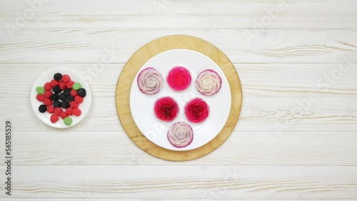 Rose shaped jelly dessert made from raspberries and cream in a white plate on a white wooden table. The chef puts a plate of dessert on the table. Round wooden board.