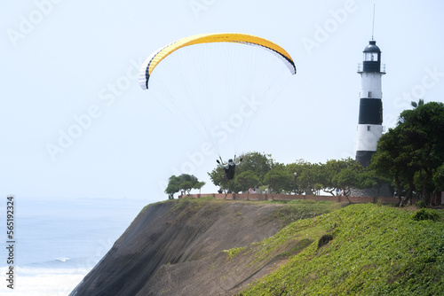 Paragliding is action sport in Lima Peru. Person is paragliding in Miraflores Lima Peru with lighthouse and buildings background.. Selective focus. Open space area.  photo