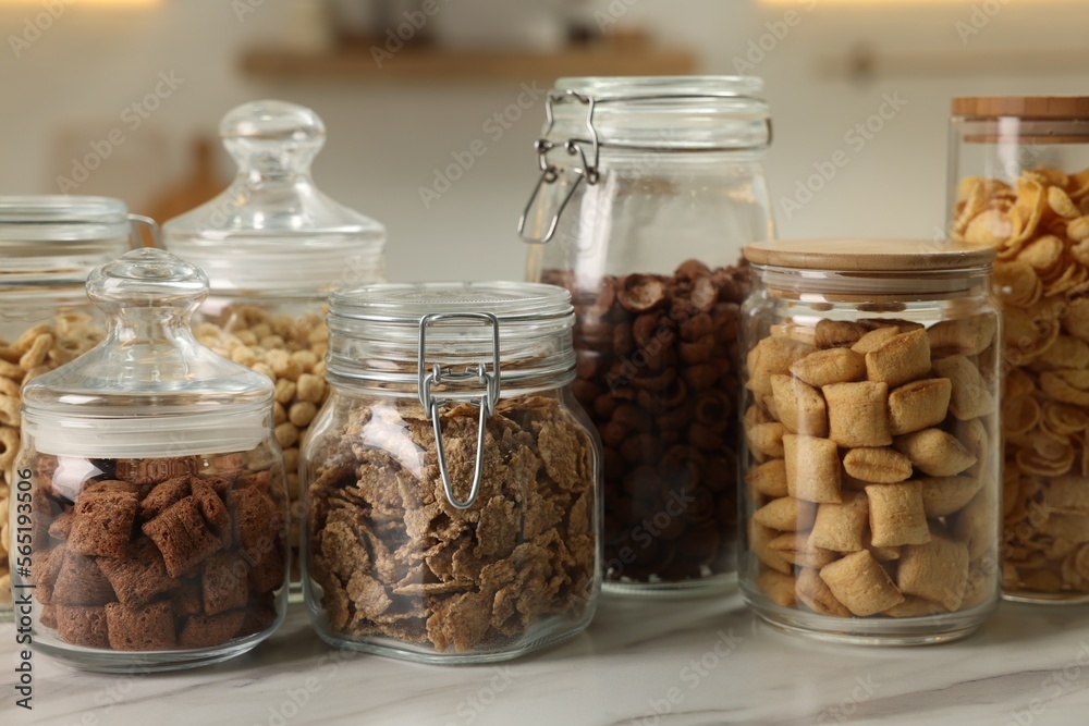Glass containers with different breakfast cereals on white marble table in kitchen Glass containers with different breakfast cereals on white marble table in kitchen