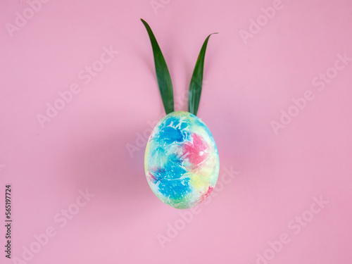 Colorful Easter Egg with Bunny Ears from green grass on pink Background. Creative Greeting Card. Minimalism Concept. Copy Space.