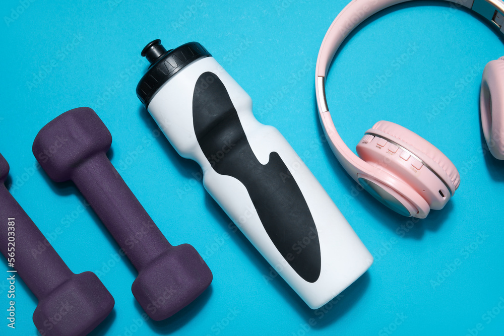 Sports water bottle with dumbbells and headphones on blue background