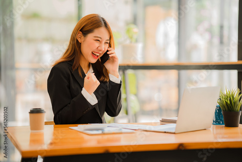 Asian female accountant working on paperwork at office while talking on the phone Writing notes on colorful sticky paper in office work with statistics Consult customers over the phone.