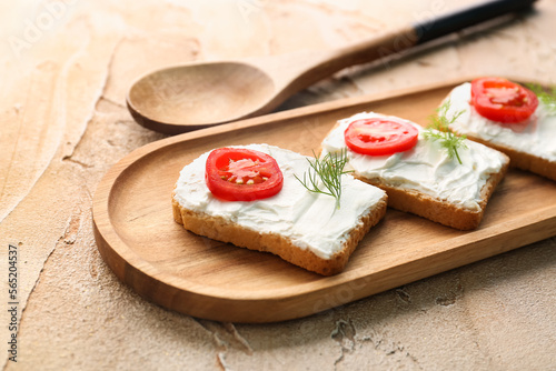 Tableau sur toile Wooden board of bread rusks with cream cheese and tomatoes on color background,