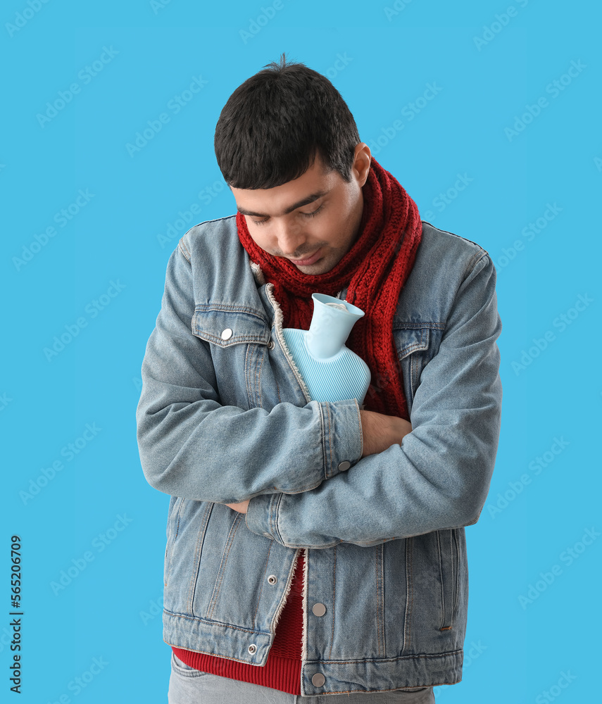 Young man warming with hot water bottle on blue background Young man warming with hot water bottle on blue background