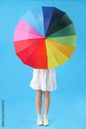 Young woman with rainbow umbrella on blue background