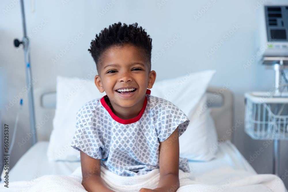 Happy african american boy patient sitting up in hospital bed, smiling with copy space Happy african american boy patient sitting up in hospital bed, smiling with copy space