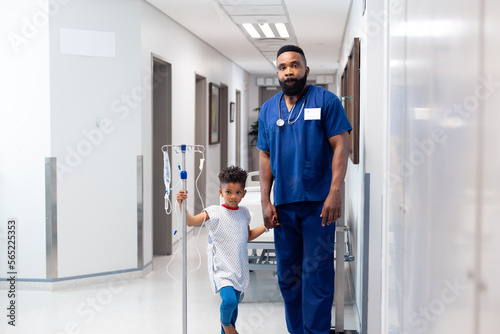 African american male doctor holding hand of boy patient with drip in hospital with copy space