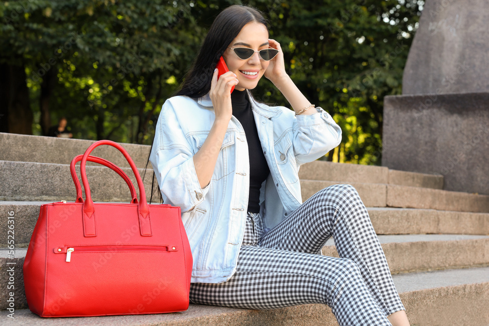 Young woman with stylish bag talking on phone outdoors