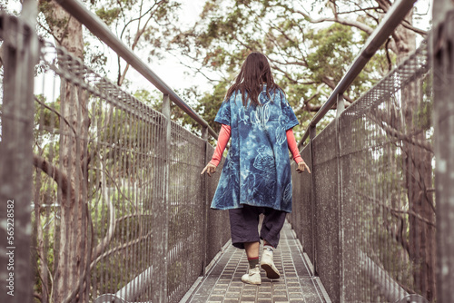 androgynous stylish figure runs fingers along railing on tree top walk photo