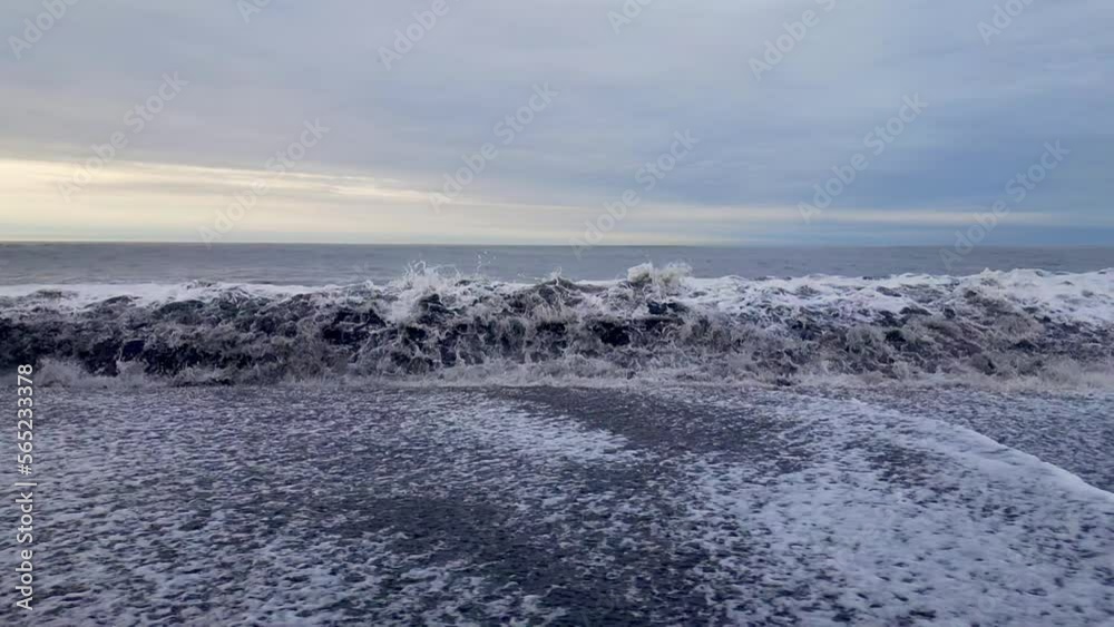 Surf waves forming white foam crashing onto a black sandy beach. Surf waves forming white foam crashing onto a black sandy beach.