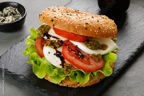 Sandwich, toast, bagel with mozzarella cheese, pesto sauce, tomatoes. Caprese Sandwich on black slate board. Fresh and healthy homemade toast.