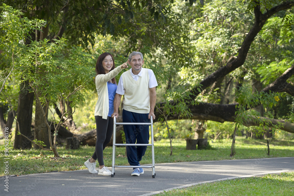 Fototapeta premium disabled senior man walking with walker, happy family, father and daughter enjoy talking and exercising in the public park, concept of daughter helps disabled father to exercise, elderly health care