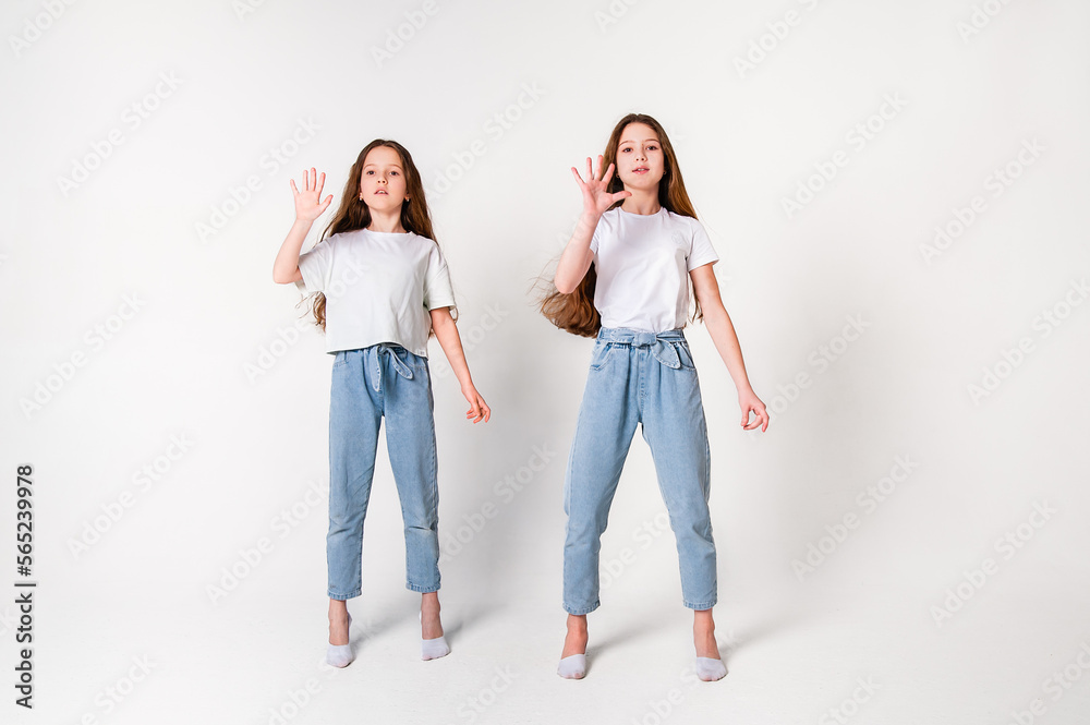 Two girls in white t-shirts and jeans stand on tiptoes and show five fingers. White background Two girls in white t-shirts and jeans stand on tiptoes and show five fingers. White background