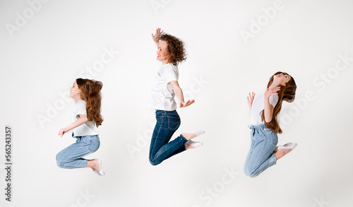 Mom and two teenager daughters in jeans and white t-shirts are smiling and happy. The three of them jump up. White background.