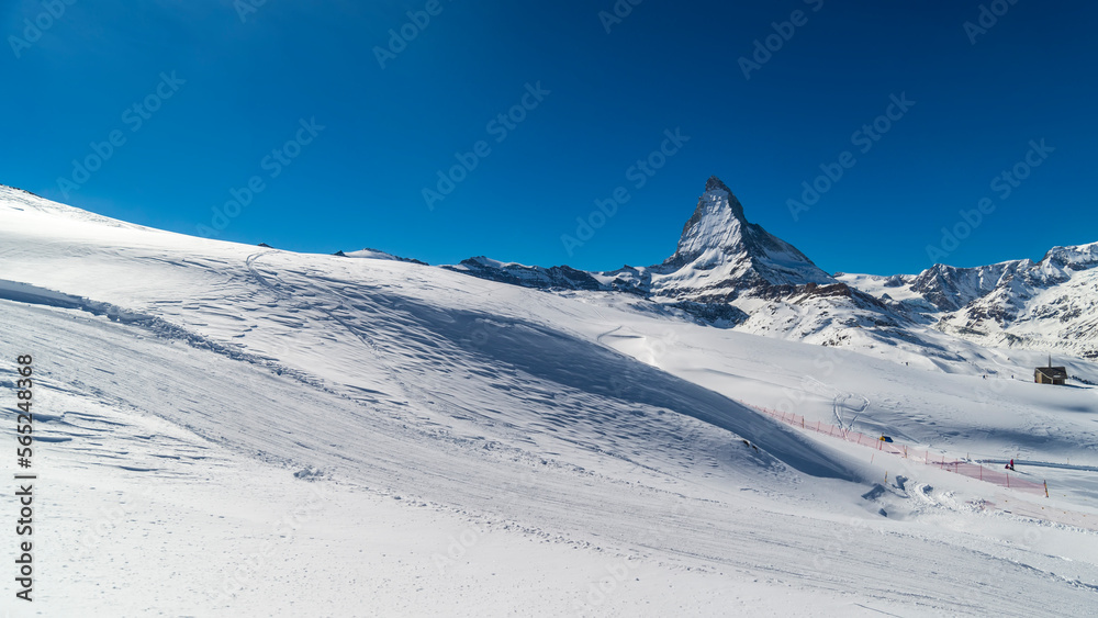 Fototapeta premium Ski slope in Swiss Alps in sunny day,Matterhorn behind. Small wooden house near by ski slope.Mountains and skiing resort for winter travel.Winter landscape of Switzerland.Zermatt winter landscape.