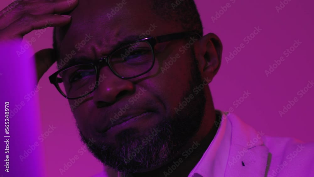 Close up View of Black Businessman Sitting at Desk Working on Laptop Computer. African American Man in Studio With Violet Magenta Background is Thinking About The Implementation of the idea. Close up View of Black Businessman Sitting at Desk Working on Laptop Computer. African American Man in Studio With Violet Magenta Background is Thinking About The Implementation of the idea.