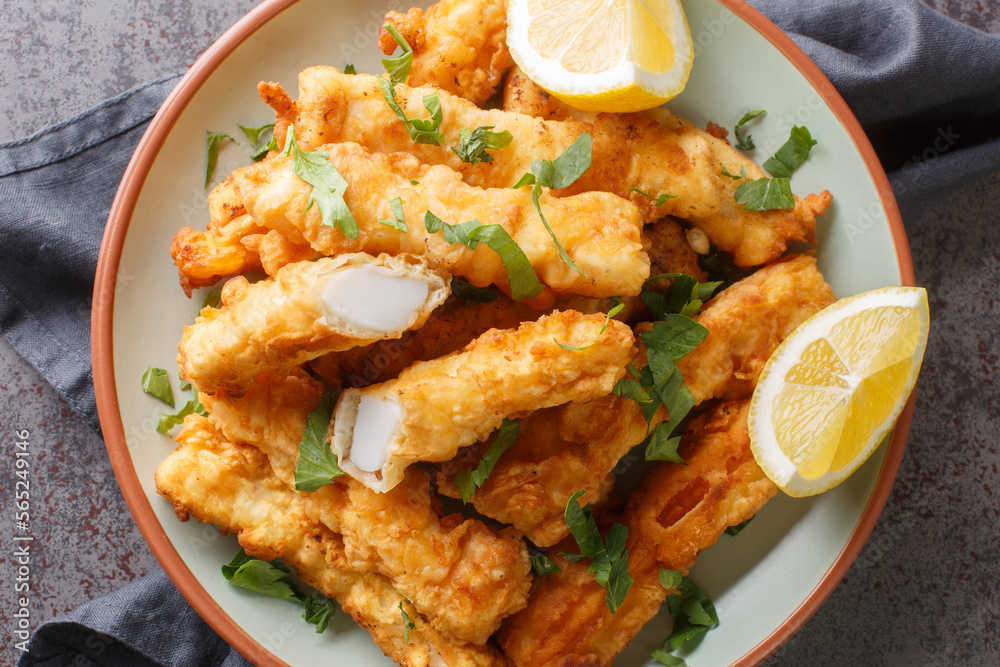 Hot breaded calamari strips served with lemon wedges closeup on the plate on the table. Horizontal top view from above Hot breaded calamari strips served with lemon wedges closeup on the plate on the table. Horizontal top view from above