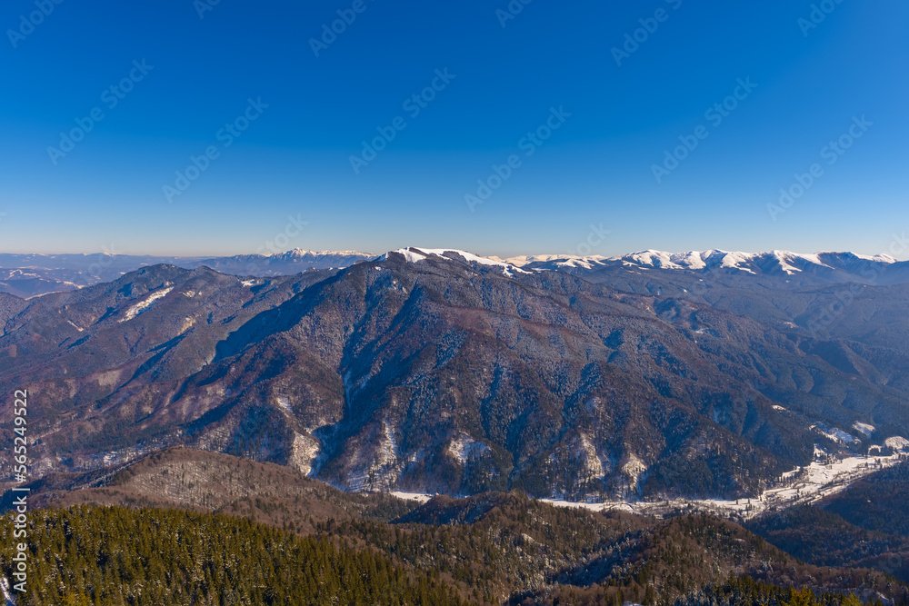 Panorama of the Piatra Mare massif, Brasov, Romania, Prahova Valley below, and the Ciucas Mountains in the background. Beautiful alpine winter panoramic view, snow capped mountains in background