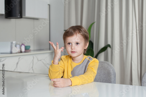 Portrait of adorable cute child boy in yellow sweater sitting by the table on white studio background