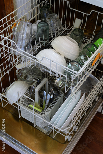 Open unattended full kitchen dishwasher with clean glasses plates and cutlery waiting to be emptied 