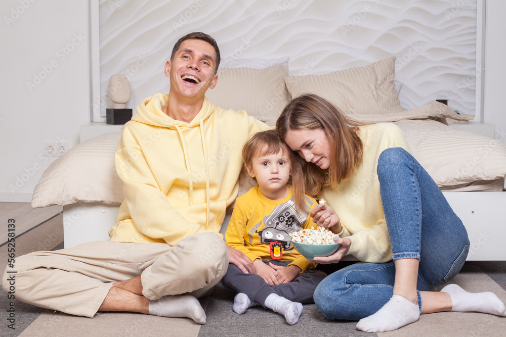 Laughing friendly family,  parents with child son sitting by the bed and eating popcorn