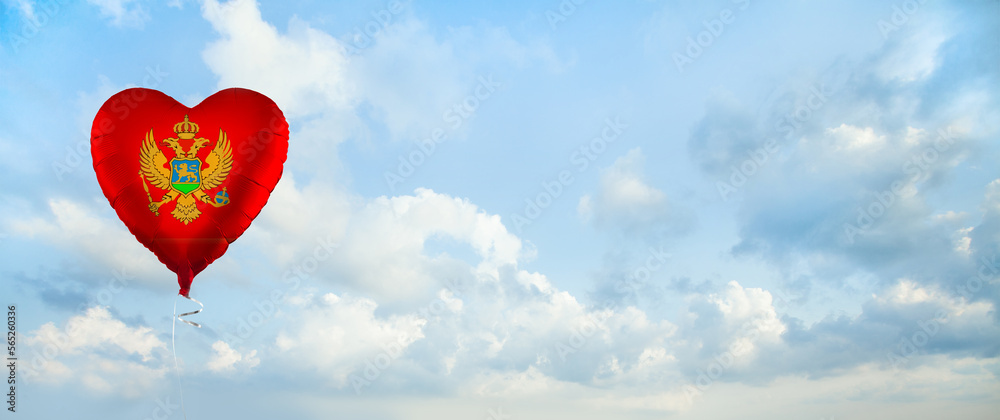Fototapeta premium Flag of Montenegro on heart-shaped balloon against sky clouds background. Education, charity, emigration, travel and learning. Montenegro language concept