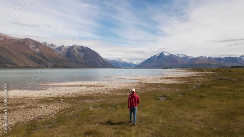 Person from behind walking along picturesque alpine lake in New Zealand. Wide angle tracking shot photo