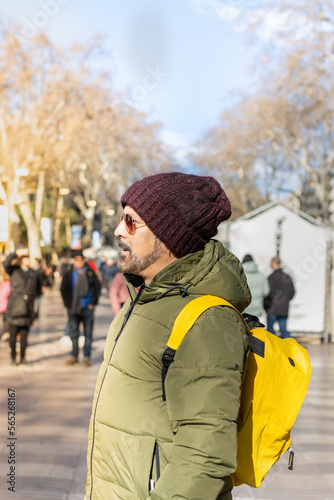Tourist with winter clothes and yellow backpack amazed on the Rambla in Barcelona (Spain).