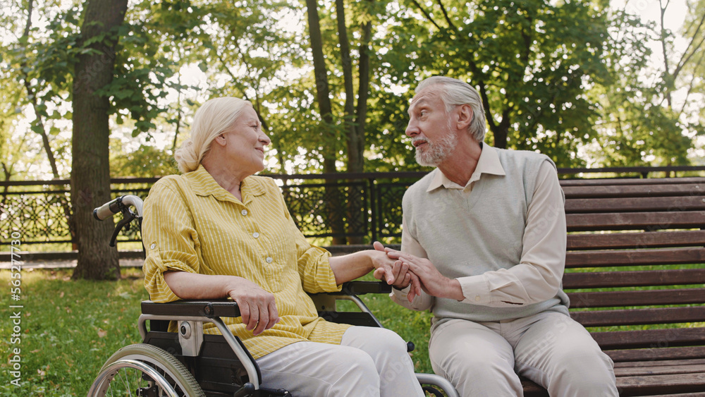 Attentive husband talking to wife with reduced mobility, stroking hand with love Attentive husband talking to wife with reduced mobility, stroking hand with love