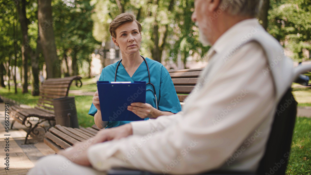 Physician writing in patient's card, talking to aged man in wheelchair, medicine Physician writing in patient's card, talking to aged man in wheelchair, medicine