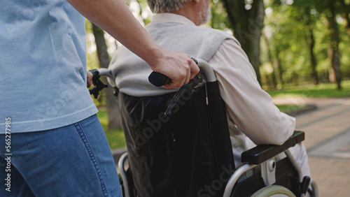 Caretaker pushing senior man's wheelchair, life with disability, retirement