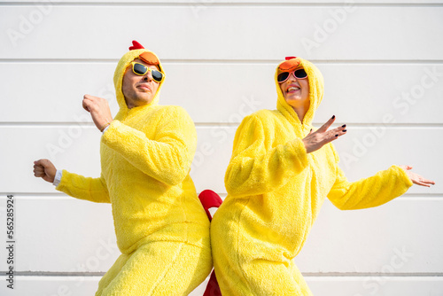 Happy woman and man wearing yellow chicken costumes having fun in front of wall