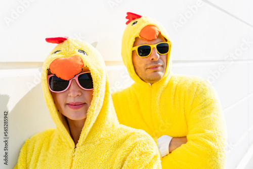 Smiling friends wearing chicken costumes and sunglasses leaning on wall photo