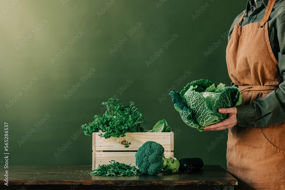 Woman wearing apron holding cabbage in front of green wall Stock Photo ...
