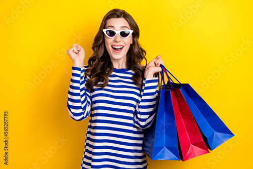 Photo portrait of lovely young lady holding shopping bags celebrate sales dressed stylish striped look isolated on yellow color background