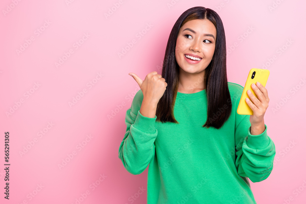 Photo portrait of dreaming interested korean lady wear green jumper hold phone look direct finger mockup new app isolated on pink color background Photo portrait of dreaming interested korean lady wear green jumper hold phone look direct finger mockup new app isolated on pink color background