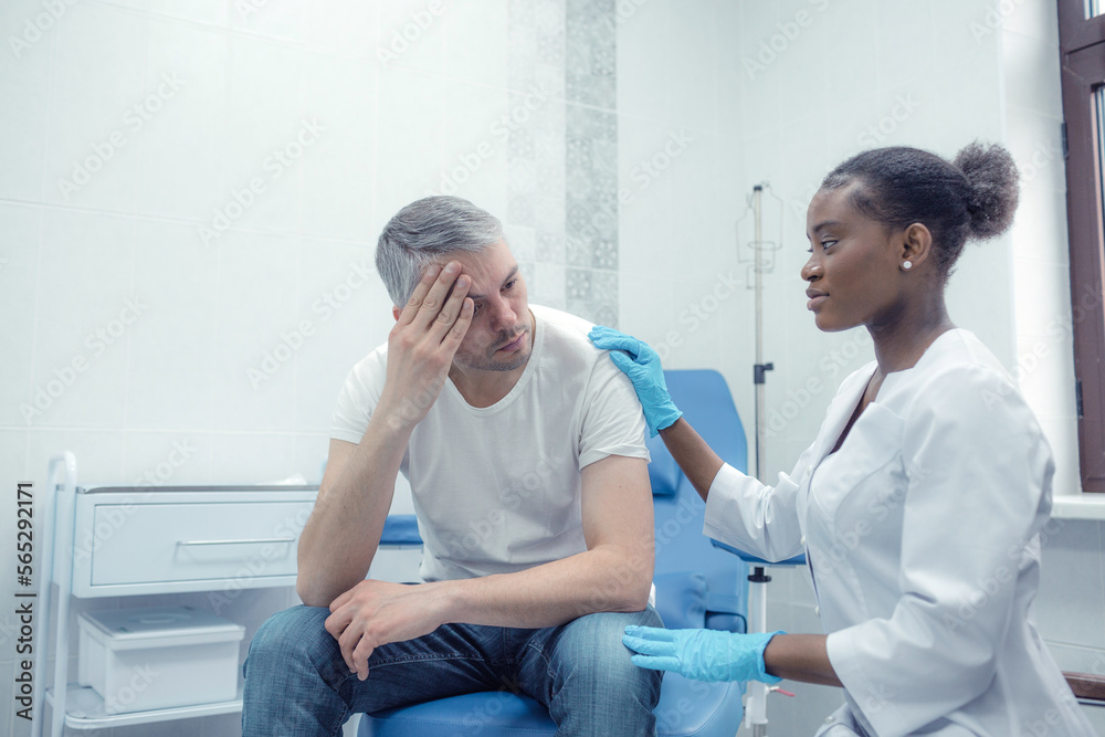 Obraz premium An unhappy adult man suffering from pain, severe headache, stress, ocular migraine, sits in a room and asks a doctor for a check and help in treatment.