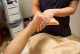 Medical worker in physiotherapy room massages client feet with his fingers