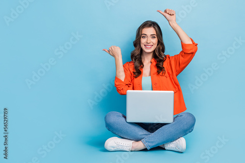Full size photo of pretty girl point empty space laptop apple macbook samsung dressed stylish orange look isolated on blue color background © deagreez