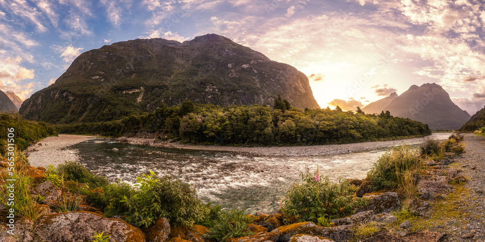 Obraz premium Panoramic view of the sun setting behind the mountains towering above the Cleddau river valley at Milford Sound in the South Island of New Zealand