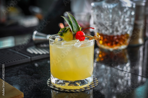 A Signature yellow drink decorated with fresh pineapple and red cherry stem in a restaurant Bangkok Thailand