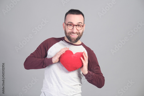 Young man holding a small red heart shaped pillow while looking at camera © Xavi