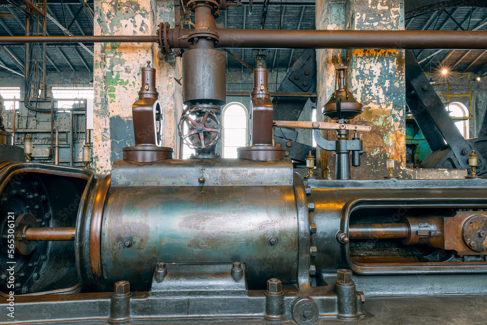 Fragment of steam engine from 1903. Important part of technological line in historical factory. Huge piston and .centrifugal regulator. Fragment of .flywheel in the background.
