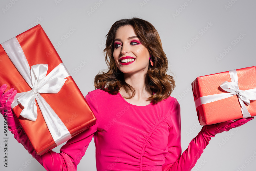 happy young woman in magenta color dress and gloves holding presents isolated on grey. happy young woman in magenta color dress and gloves holding presents isolated on grey.