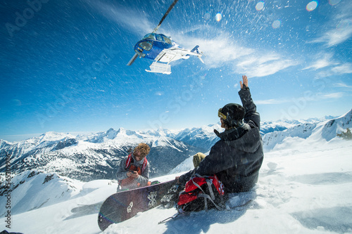 Snowboarders watching a heli take off after being dropped off on a remote peak in the backcountry