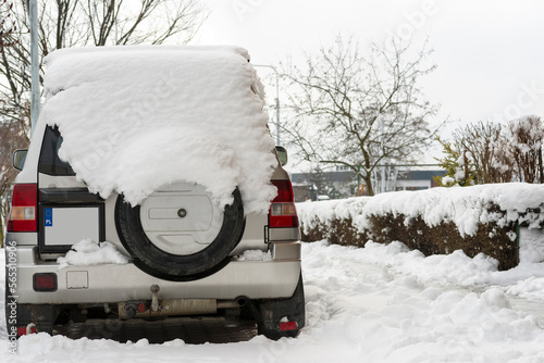 Mały , terenowy samochód produkcji japońskiej , pokryty sporą ilością śniegu , zaparkowany na zaśnieżonym parkingu osiedlowym .